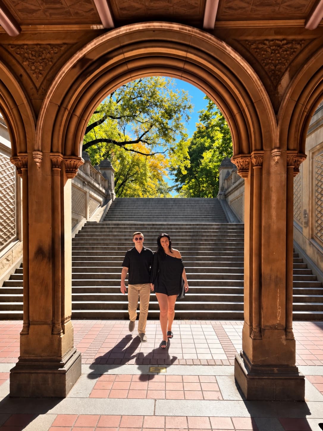 Kenzie and Tyler walking hand in hand under the arches of Bethesda Terrace in Central Park