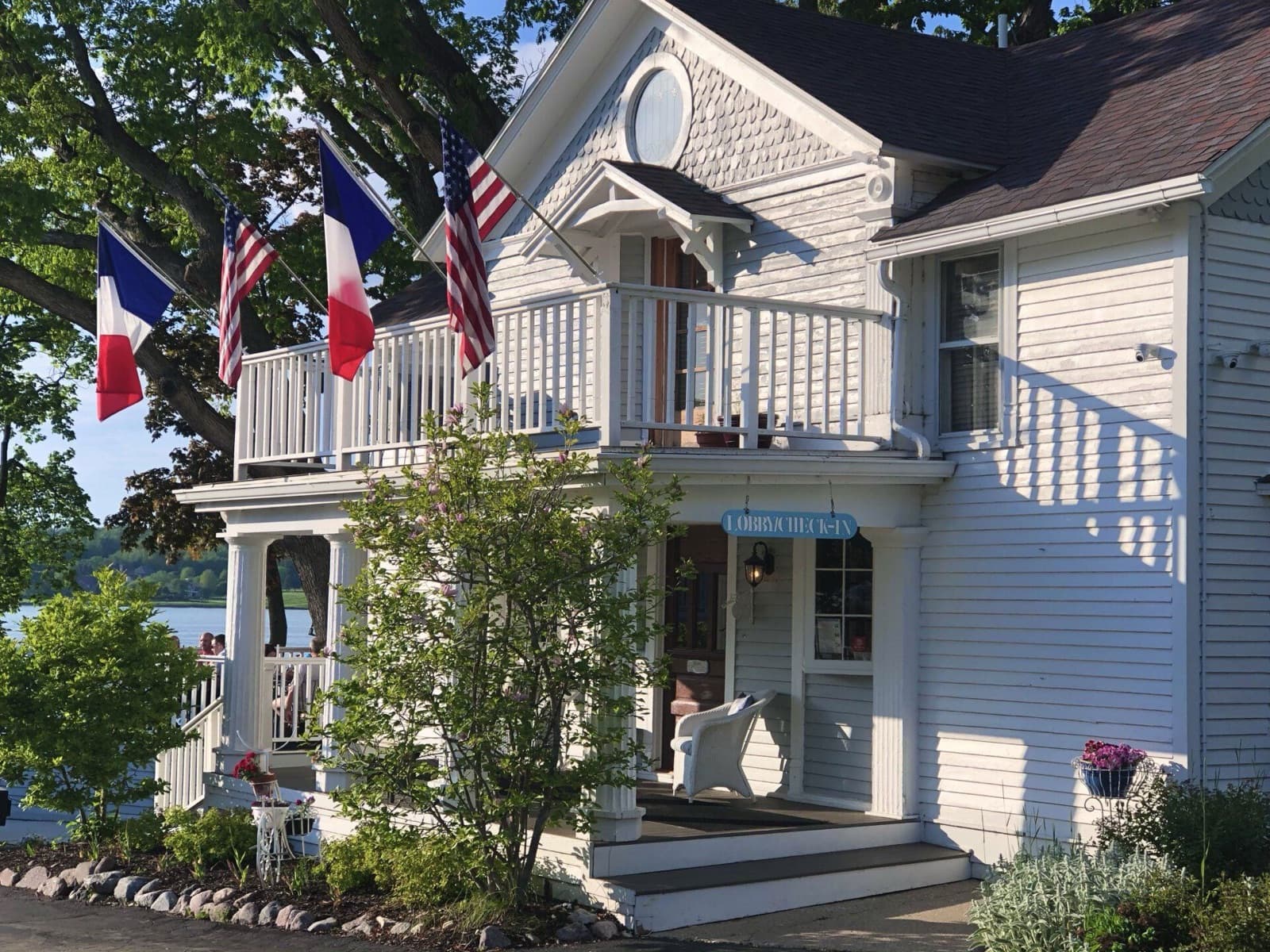 The white clapboard porch of The French Country Inn, flying French and American flags beside the lake